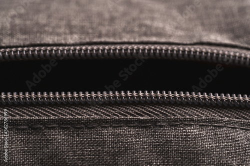 Horizontal opened zippers of gray cloth bag in low light mood