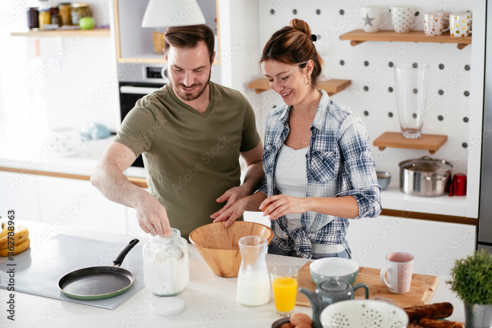 Young couple making pancakes together at home. Loving couple having fun while cooking. Young couple making pancakes together at home. Loving couple having fun while cooking.