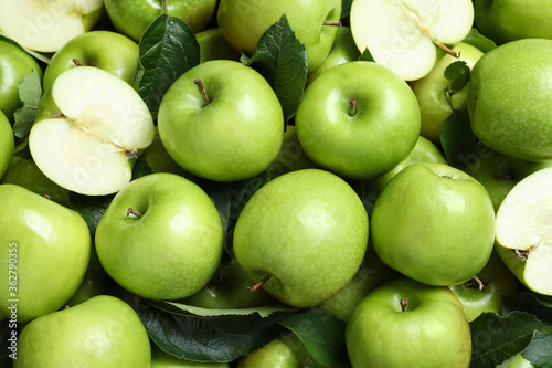 Pile of tasty green apples with leaves as background, top view