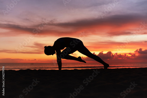Fototapeta Naklejka Na Ścianę i Meble -  Yoga Poses. Woman Practicing Cat Stretch Asana On Ocean Beach. Female Silhouette Standing In Marjariasana Pose At Beautiful Sunset. Yoga As Exercise For Lifestyle.