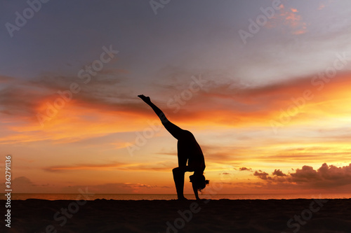 Yoga Poses. Woman Standing Split Asana Or One Foot Up Pose On Ocean Beach. Female Silhouette Practicing Urdhva Prasarita Eka Padasana At Beautiful Sunset. Yoga As Exercise For Lifestyle.