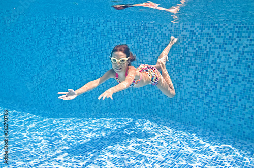 Child swims underwater in swimming pool  happy active girl dives and has fun under water  kid fitness and sport on family vacation on resort 