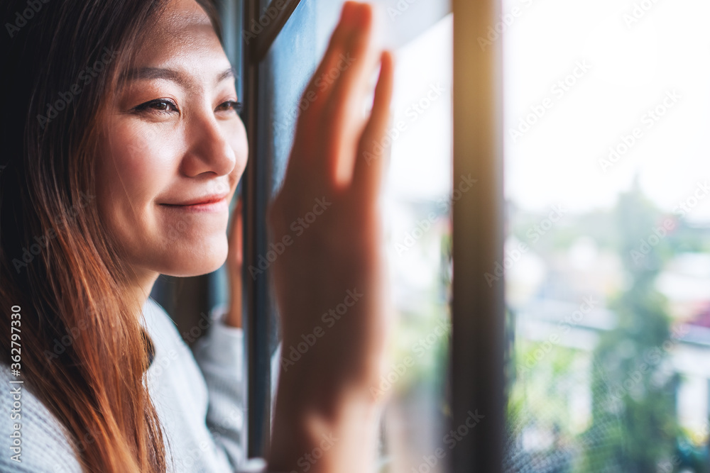 Closeup image of a young woman touching on window while looking outside