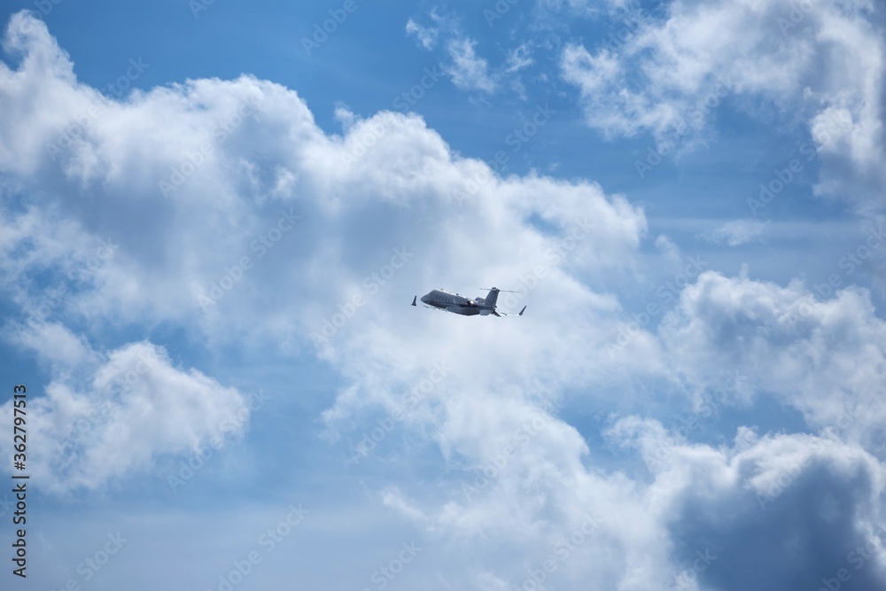 Small silhouette of business jet airplane after taking off on grey white clouds in blue sky background. Fast modern aircraft for air transportation. Aviation technology. Travel and business concept.