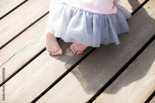 The legs of a little toddler crawling on a wooden floor in a park for a walk on a summer's final day.
