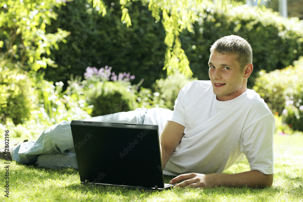 Teenage boy lying on the field using laptop