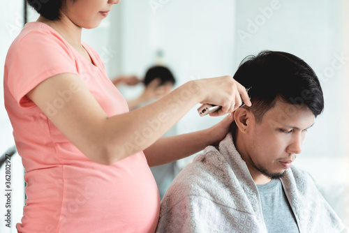 Young Pregnant Woman cutting husband hair with clipper at home