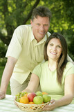 Couple sitting at the picnic table with a basket of fruits