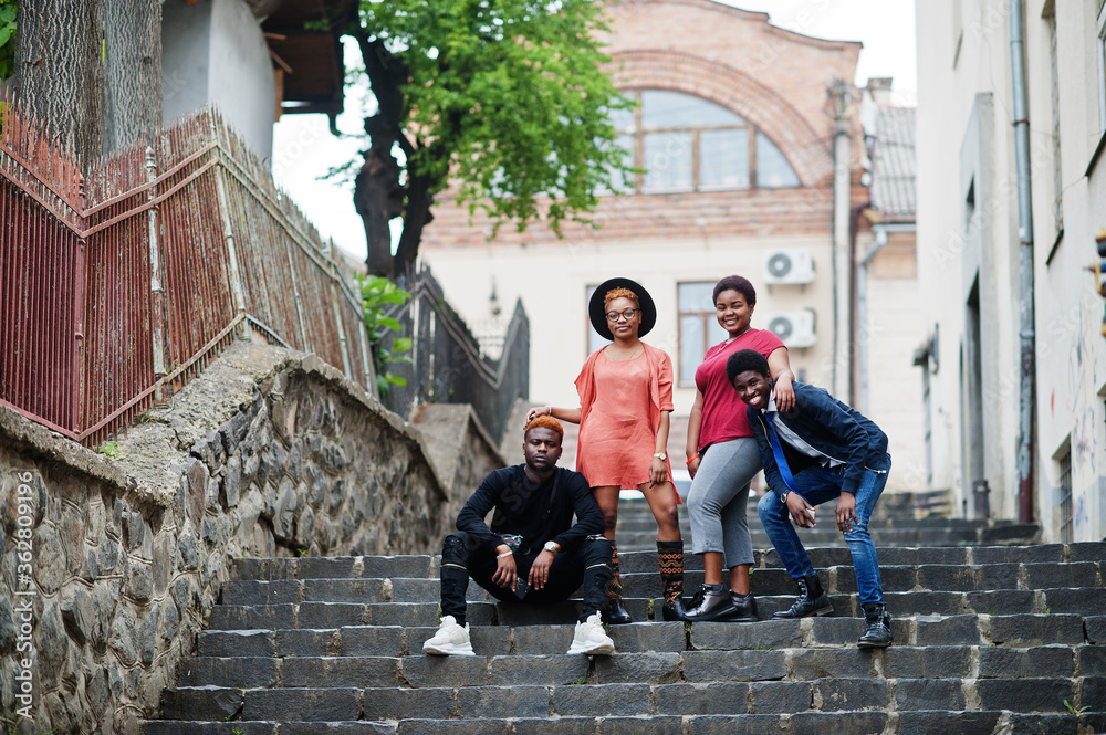 Four african friends having fun outdoors. Two black girls with guys sit on stairs of an old city.
