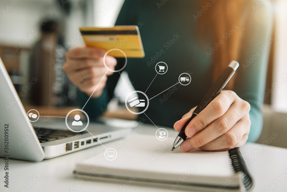 Women use credit cards to pay through laptop computer and take notes in office. Women use credit cards to pay through laptop computer and take notes in office.