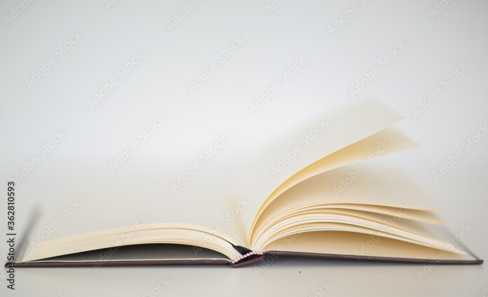 Closeup of a beautiful hardcover notebook with turning empty pages laying flat on a table. Isolated against a white background.