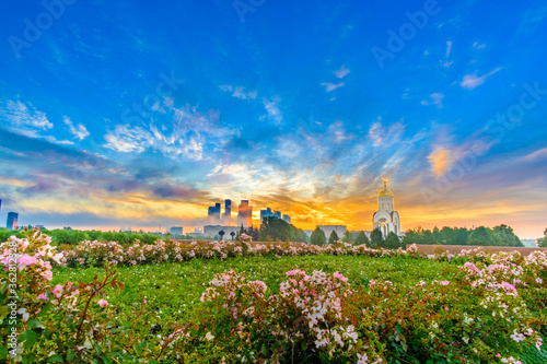 Dawn over Victory Park on Poklonnaya Hill in Moscow in the summer. Colorful blue sky with clouds and sunrise on the horizon above Moscow City skyscrapers. A carpet of flowers in the foreground.