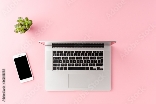 Business background with laptop, mobile phone and green flower on pink table. Office desktop. Top view