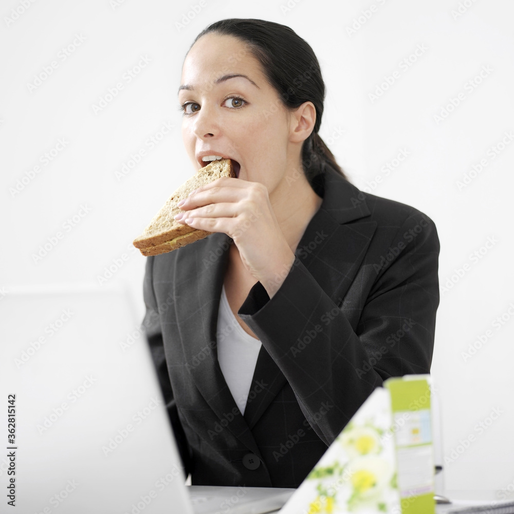 Businesswoman eating sandwich while using laptop Businesswoman eating sandwich while using laptop