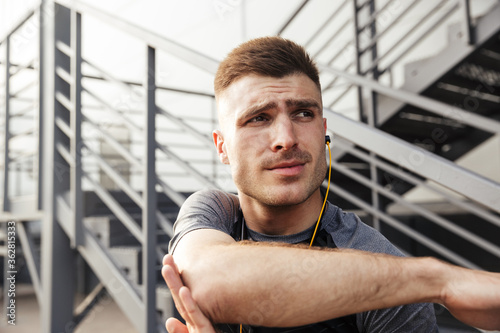 Image of unshaven athletic sportsman using earphones while working out