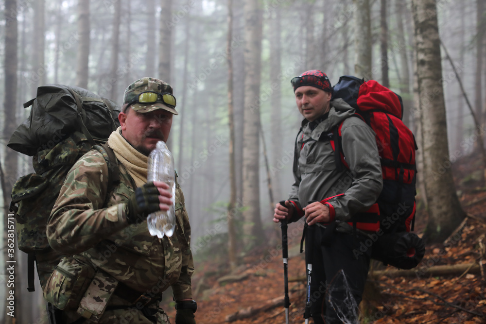 Two men hike in forest with backpack for trekking Two men hike in forest with backpack for trekking