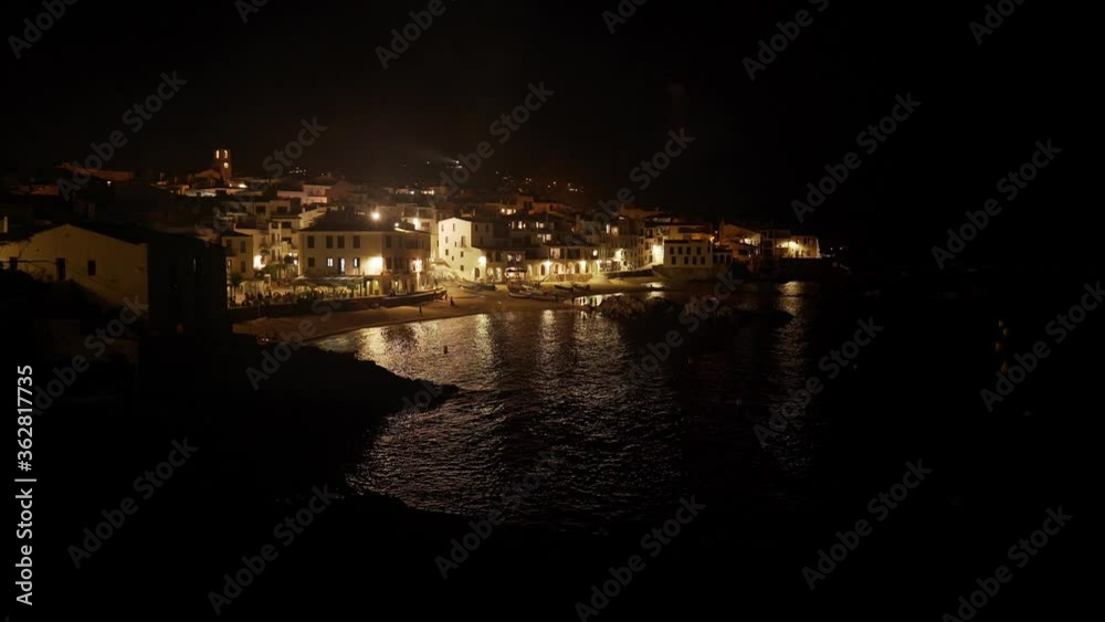 View of a beautiful coastal village at night. Small Mediterranean town. White houses on a sandy beach. Vacations on the coast. Light in the windows is reflected in the ripples of the sea. View of a beautiful coastal village at night. Small Mediterranean town. White houses on a sandy beach. Vacations on the coast. Light in the windows is reflected in the ripples of the sea.