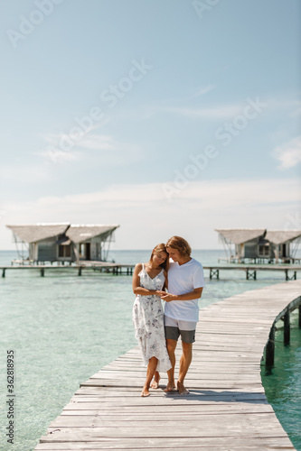 Follow me beach couple man holding girlfriend hand following woman to the swimming pool blue ocean vacation, walk together on wooden jetty