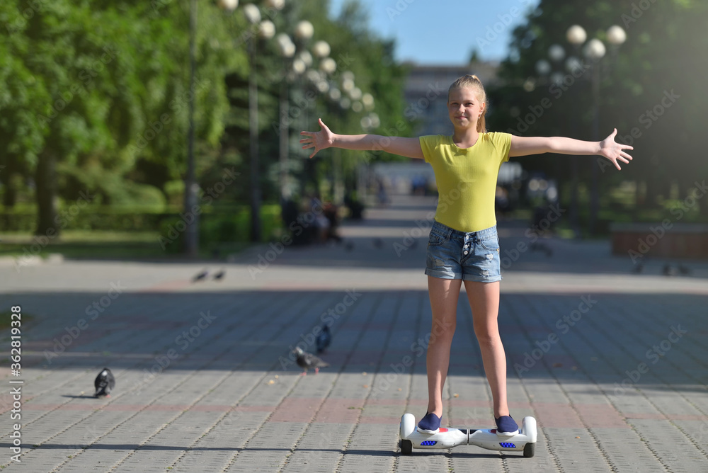 Happy teenager girl riding a hoverboard in a summer park with arms open