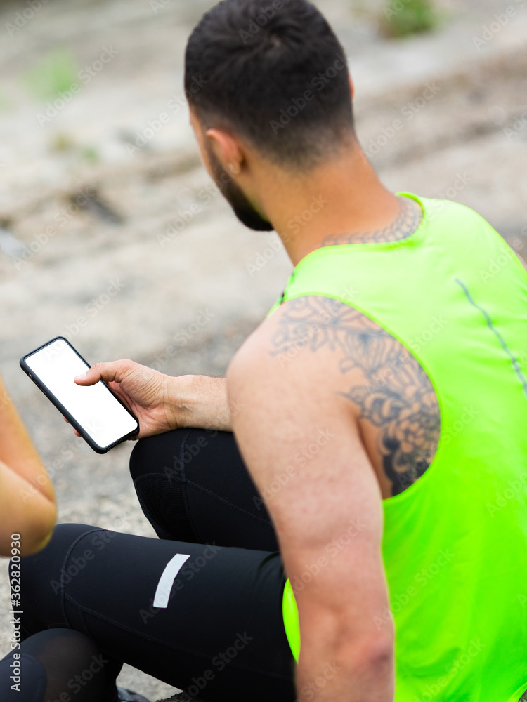 Athletic man in stylish sportswear train with phone with empty screen, photography for sport blog or app