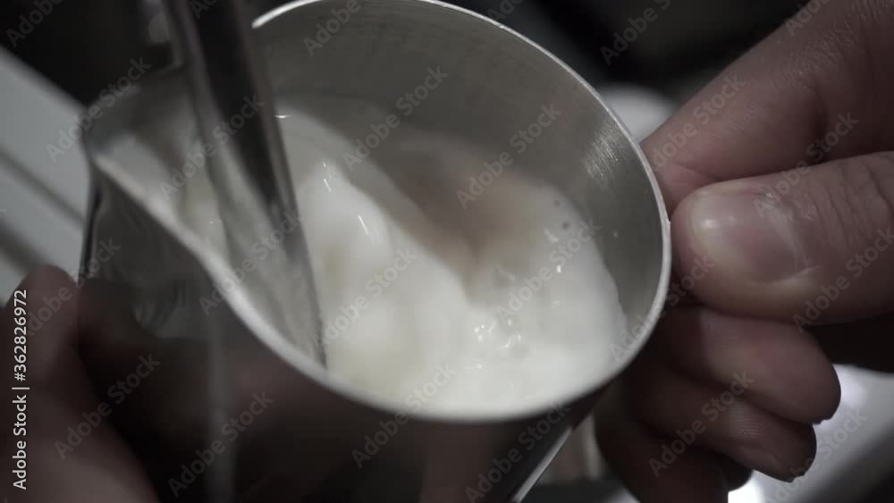 Barista foaming milk with machine. Male barista making cappuccino. Frothing Milk with a Steam Wand. Close-Up Of Barista Holding Coffee Cup.