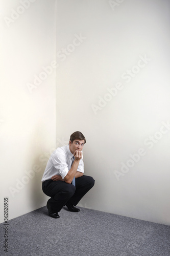 Businessman squatting down in corner of room
