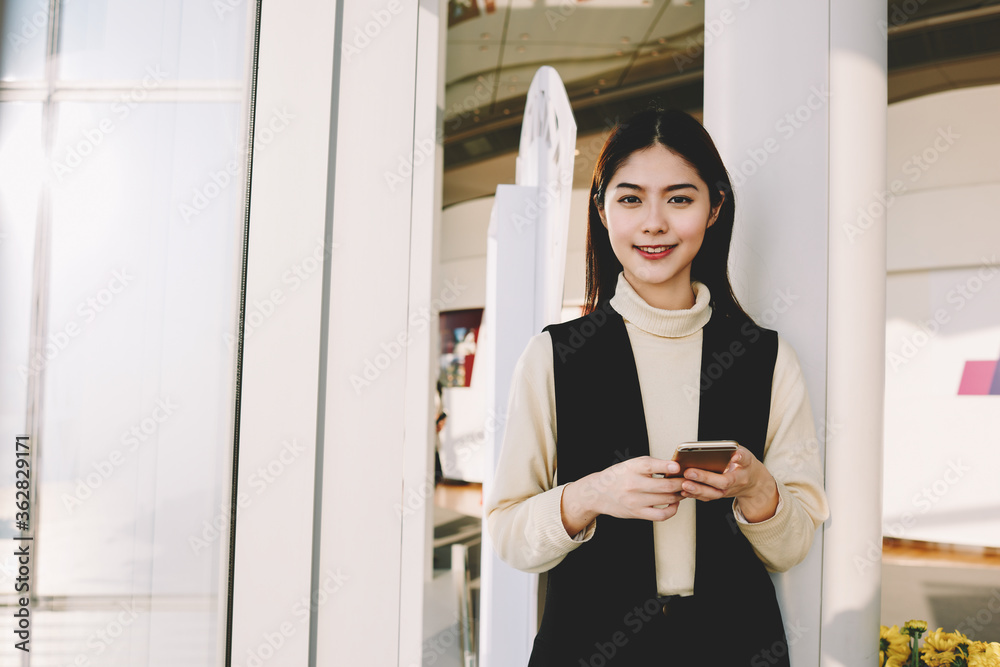 Asian woman managing director with good mood is holding cell telephone and looking in camera, while is posing for local business newspaper. Smiling hipster girl is waiting for a call on mobile phone Asian woman managing director with good mood is holding cell telephone and looking in camera, while is posing for local business newspaper. Smiling hipster girl is waiting for a call on mobile phone