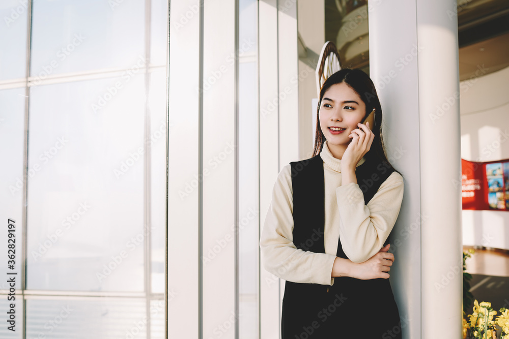 Young woman secretary having cell telephone conversation with boss during his business trip abroad about successful performance of all his tasks, while she is standing near copy space for your content Young woman secretary having cell telephone conversation with boss during his business trip abroad about successful performance of all his tasks, while she is standing near copy space for your content