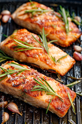 Grilled salmon fillets sprinkled with fresh herbs on a grill plate close up view