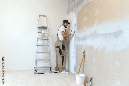 Male painter with a putty knife in his hands makes repairs