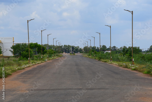 deserted lonely wide road due to pandemic lockdown with beautiful sky and street lamp post aligned perspective, symmetrical during day time in Central University of Tamil Nadu, India 
