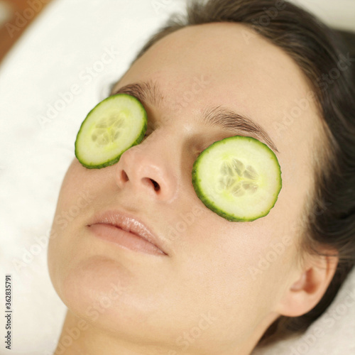 Woman lying down with sliced cucumbers covering her eyes