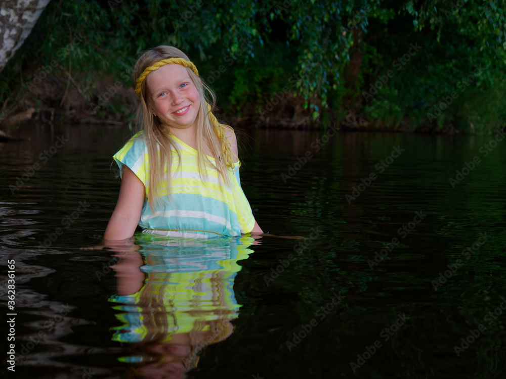 Fototapeta premium blonde girls with blue eyes bathes in clothes in the dark water of a lake at sunset