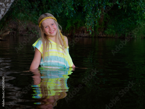 Fototapeta Naklejka Na Ścianę i Meble -  blonde girls with blue eyes bathes in clothes in the dark water of a lake at sunset