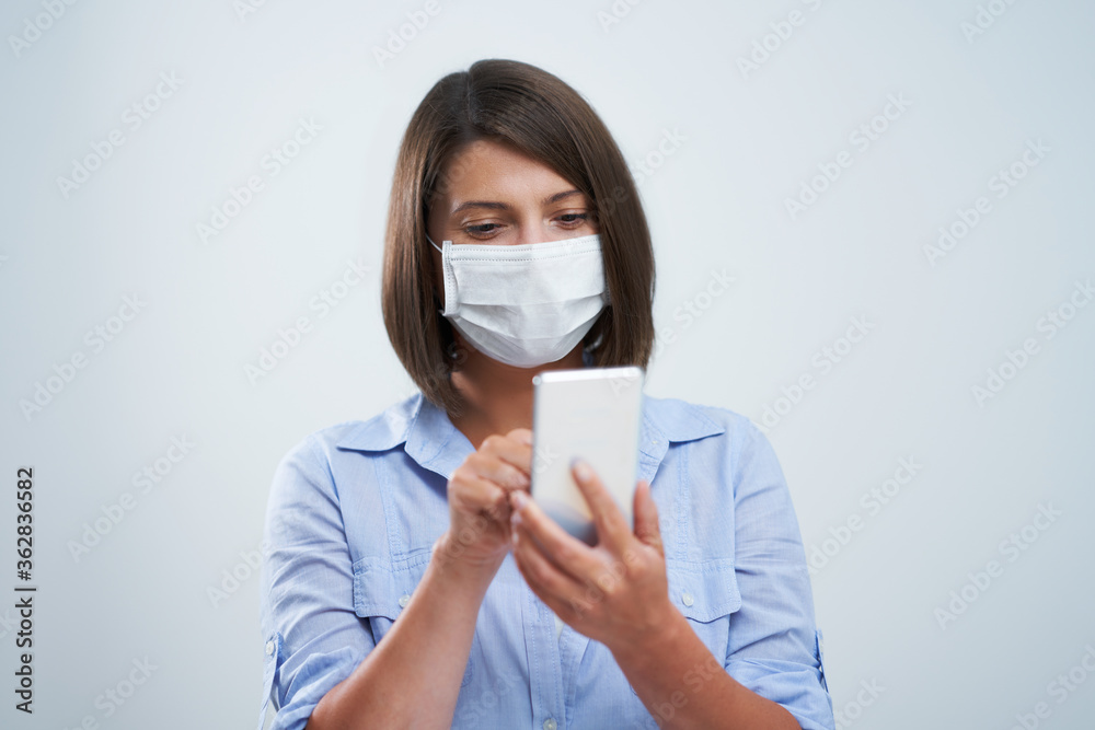 Attractive woman wearing protective mask holding smartphone isolated over white background Attractive woman wearing protective mask holding smartphone isolated over white background
