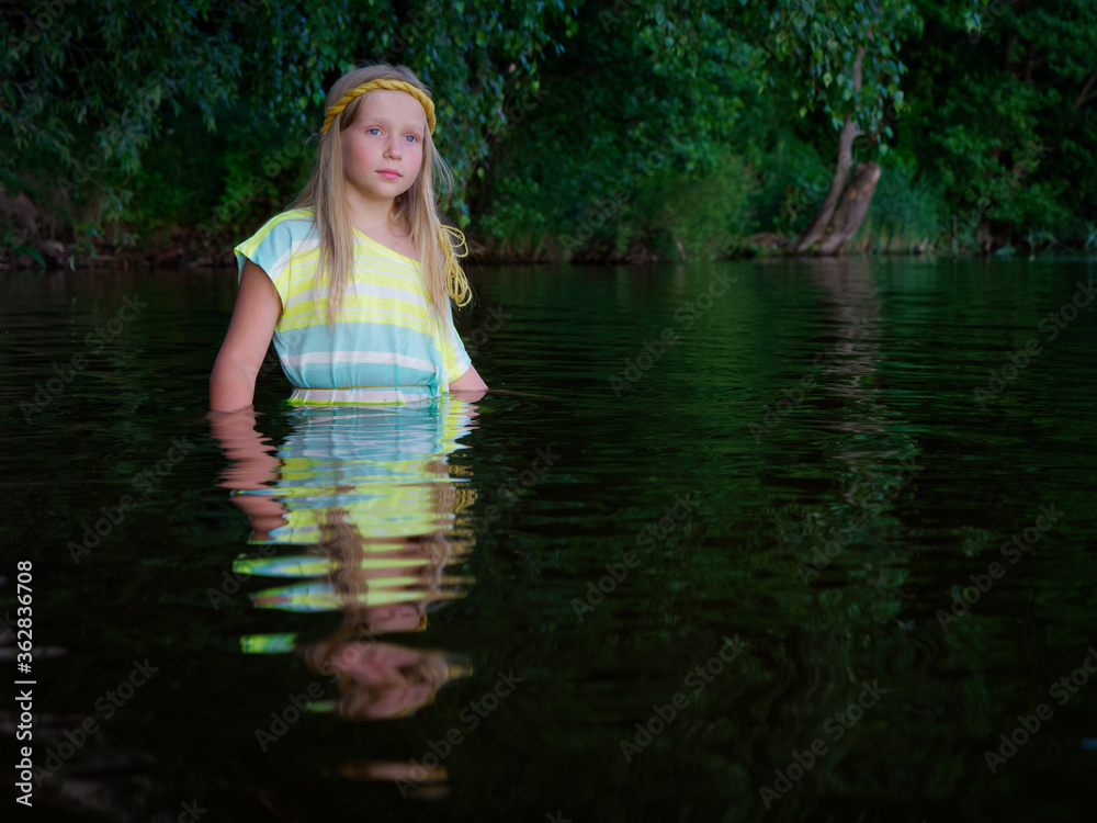 Fototapeta premium blonde girls with blue eyes bathes in clothes in the dark water of a lake at sunset