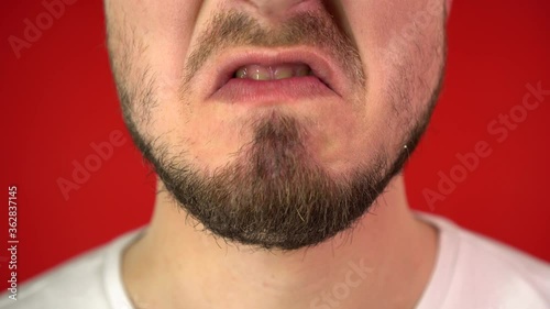Close-up mouth of angry man screaming. Threat of violence, Emotions of anger. Red Background, Studio Video, 4K, Isolate.