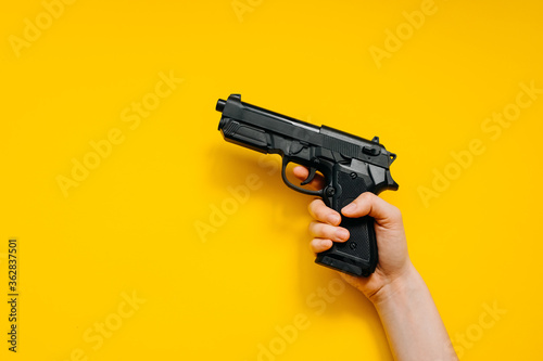 Human hand holding a gun on bright clean yellow background.