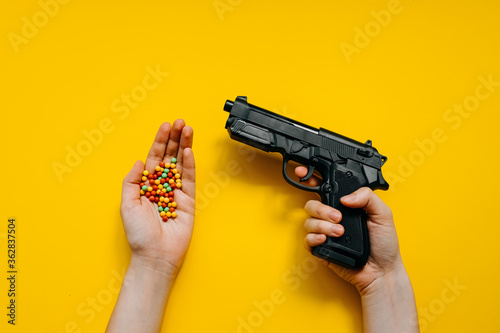 Fotografie Human hand holding a plastic toy gun and a bunch of plastic ball bullets on bright clean yellow background