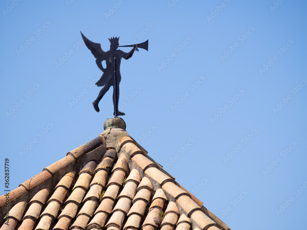 Obraz premium Antique Weather vane on the tile roof over Girona Old City in Spain. Copy Space. Man with trumpet.