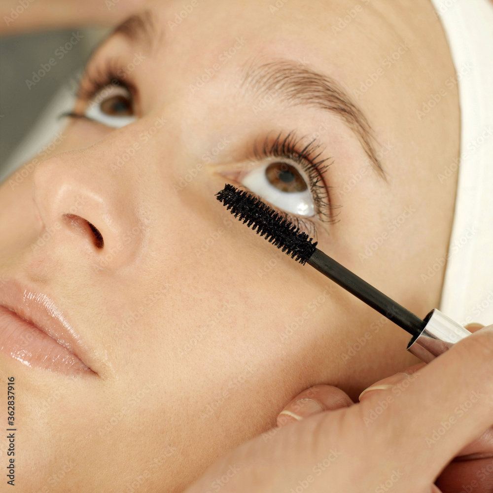 Hand curling up woman's eyelash with a mascara wand