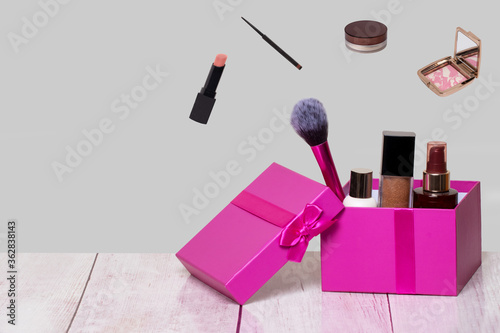 Fototapeta Naklejka Na Ścianę i Meble -  Decorative composition of colorful beauty and makeup products and tools in a pink gift box on a bright table and with further cosmetics accessories on a light gray background. Copy space for advertisi