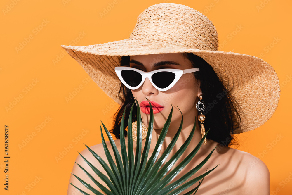Φωτογραφία stylish woman in sunglasses and straw hat near palm leaf isolated on orange