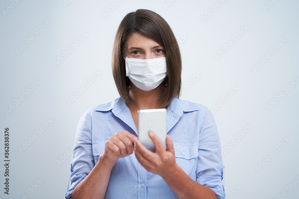 Attractive woman wearing protective mask holding smartphone isolated over white background Attractive woman wearing protective mask holding smartphone isolated over white background