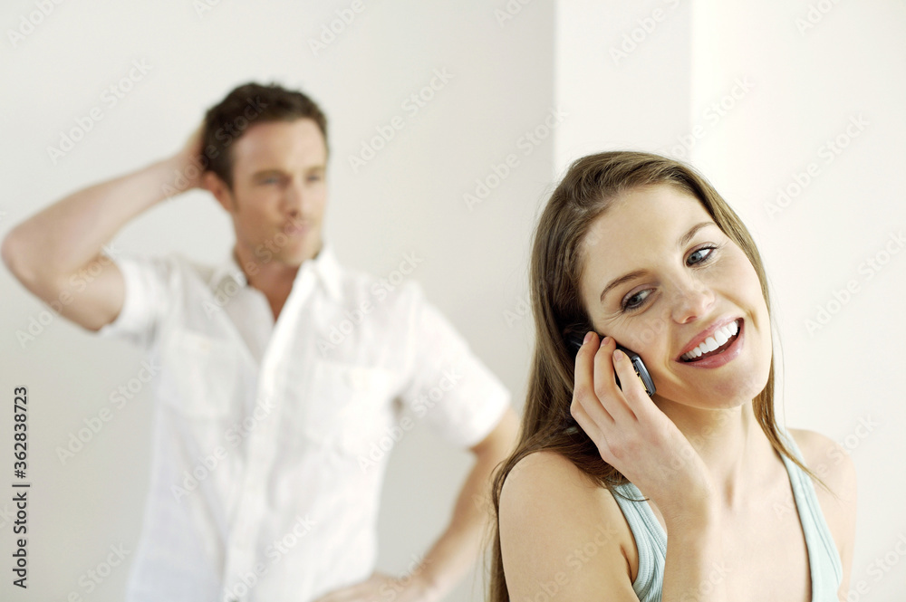 Man scratching his head while watching his girlfriend talking on the phone Man scratching his head while watching his girlfriend talking on the phone