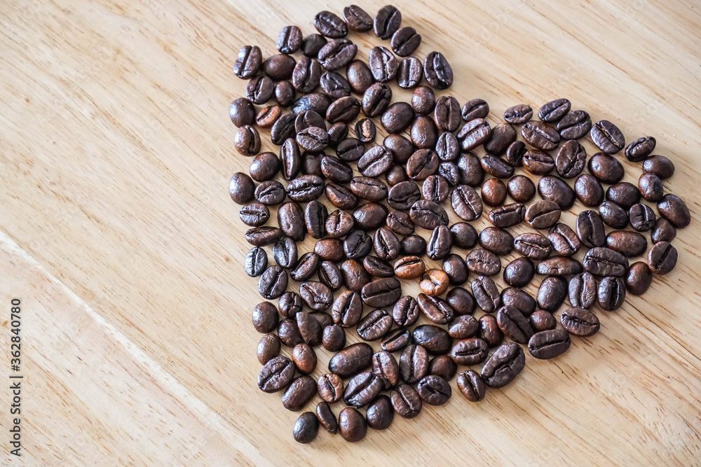 A heart-shaped made by roasted coffee beans on a light wooden background. Coffee lover concept background A heart-shaped made by roasted coffee beans on a light wooden background. Coffee lover concept background