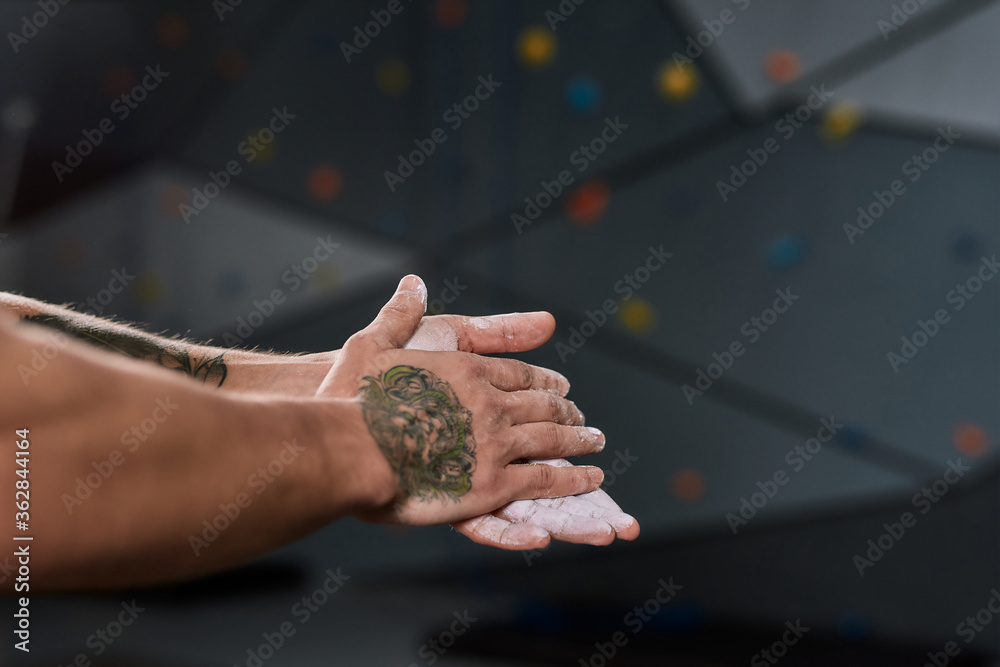 Close up of hands of man applying white dust of magnesia, chalk on hands before climbing wall in bouldering center. Concept of sport life and rock climbing Close up of hands of man applying white dust of magnesia, chalk on hands before climbing wall in bouldering center. Concept of sport life and rock climbing