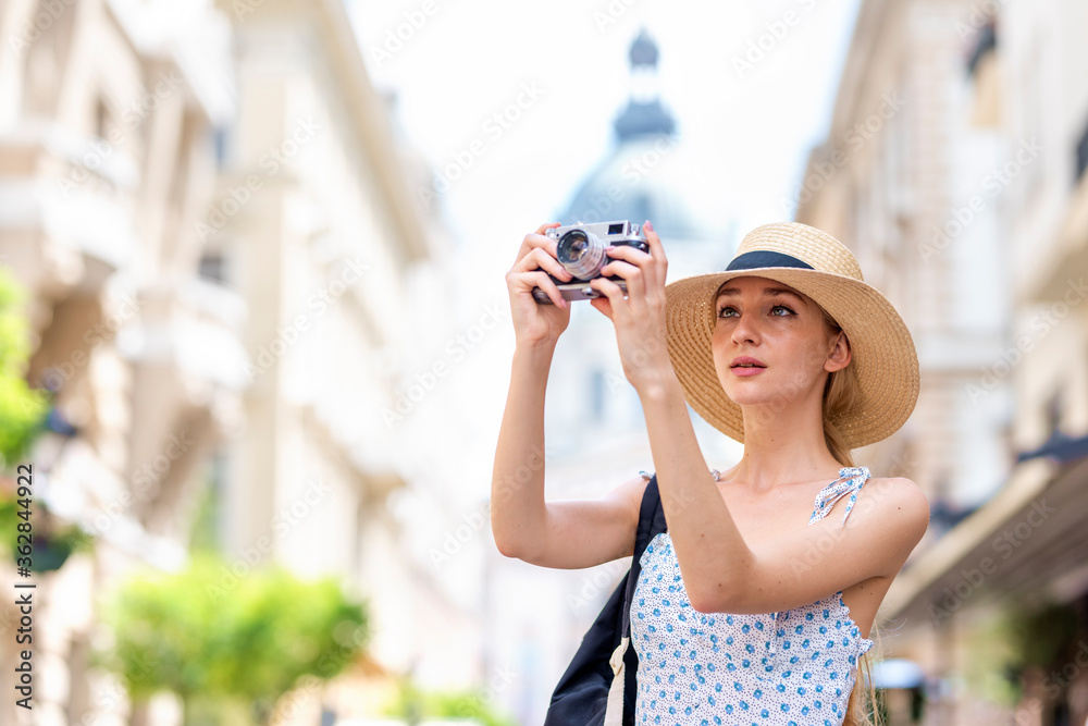 Beautiful young woman taking pictures with her camera while exploring the city