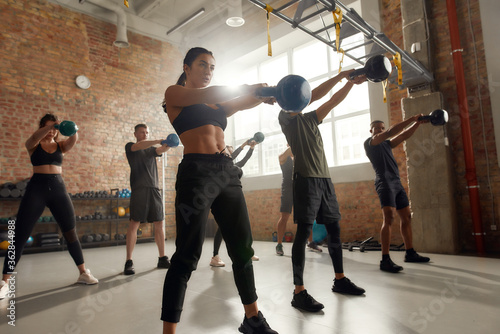 Simple. Painful. Group of sportive people lifting weight while having workout at industrial gym. Group training, teamwork concept photo