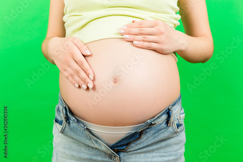 Close up of pregnant belly at colorful background with copy space. Future mother in opened jeans is embracing her naked baby bump. Motherhood concept © sosiukin